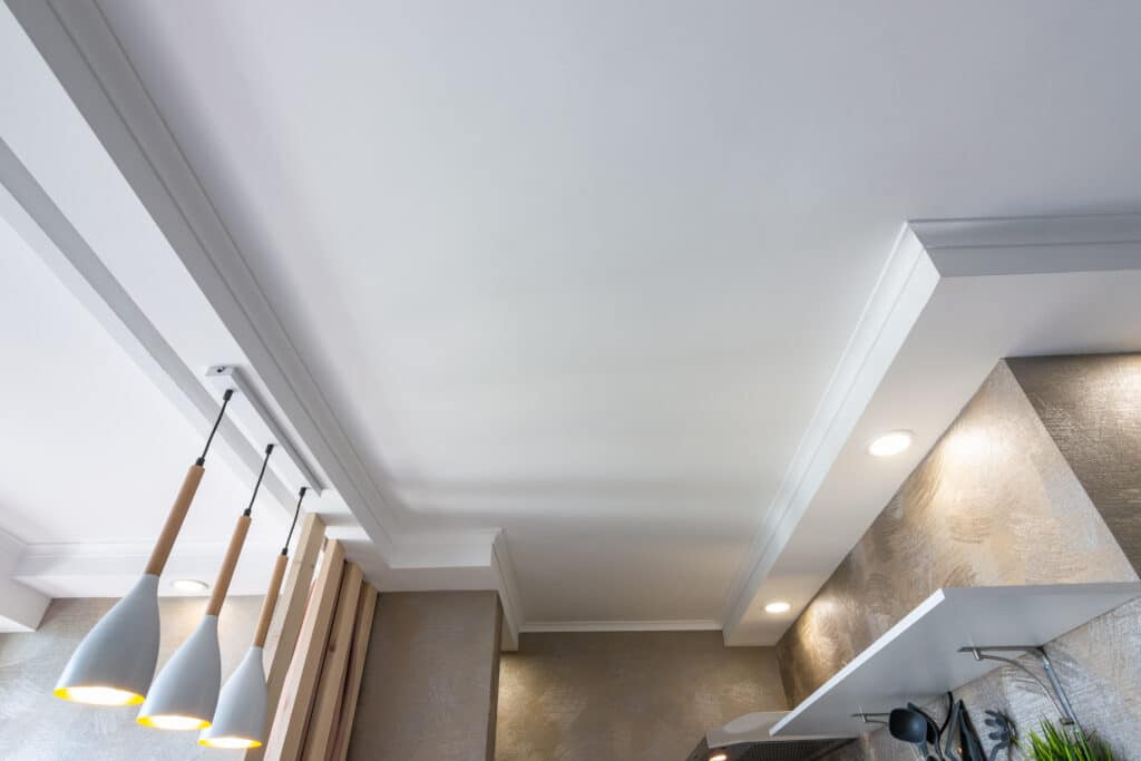 Plafond blanc moderne avec éclairage LED intégré et suspensions design. Murs texturés brillants et éléments bois.