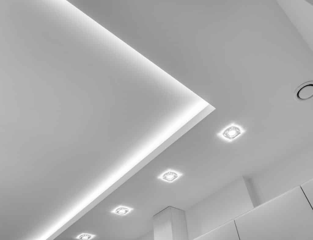 Plafond blanc moderne avec éclairage LED linéaire intégré et spots encastrés carrés, créant une ambiance lumineuse contemporaine.