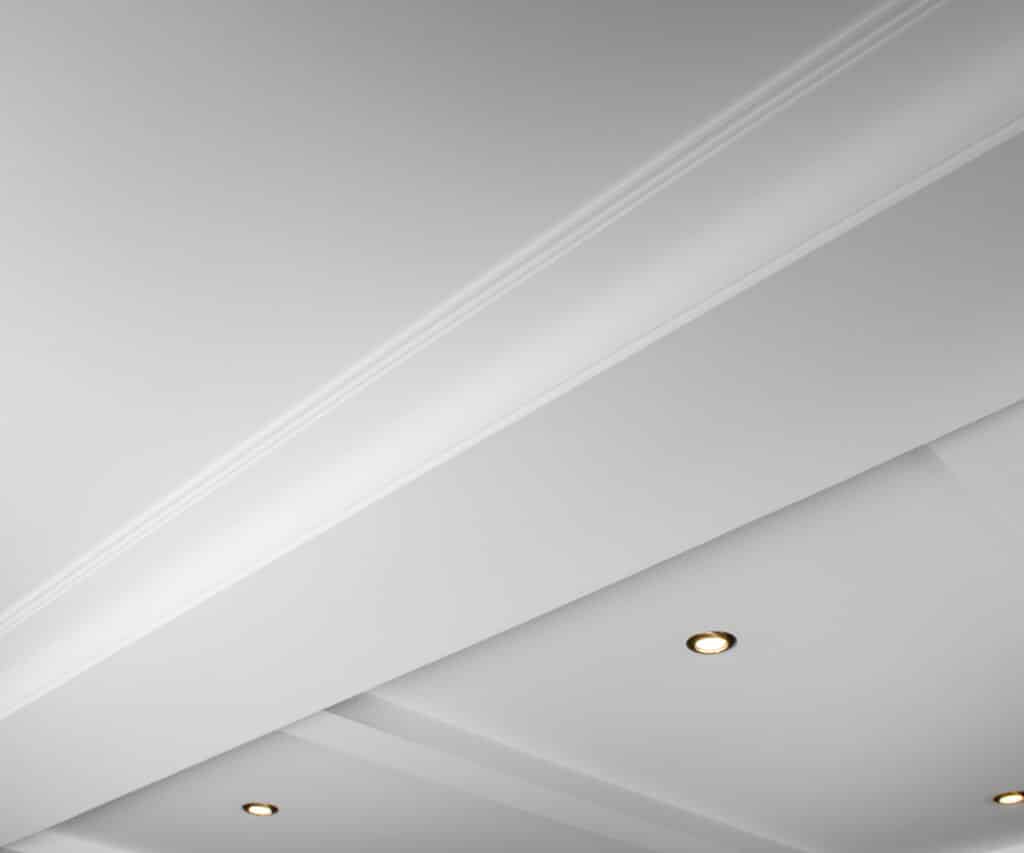 Plafond blanc moderne avec moulures décoratives et spots encastrés diffusant une lumière chaude. Design architectural élégant.
